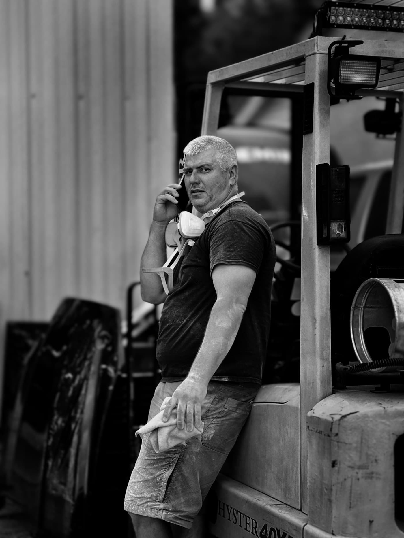 Un artisan appuyé contre un engin de chantier, le téléphone à l’oreille